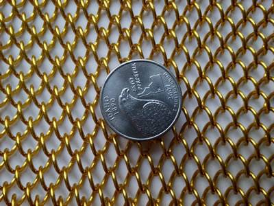 A piece of golden color coil fabric with a metal coin on its surface.